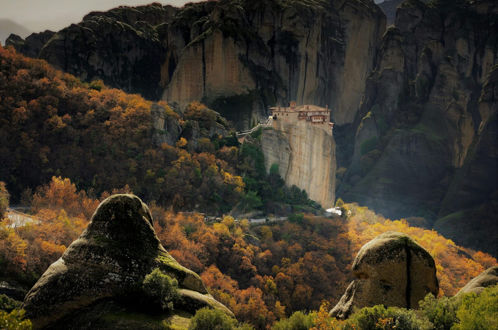 Majestic view of the Meteora Monastery perched on rocky cliffs amid autumn foliage in Kalabaka, Greece.